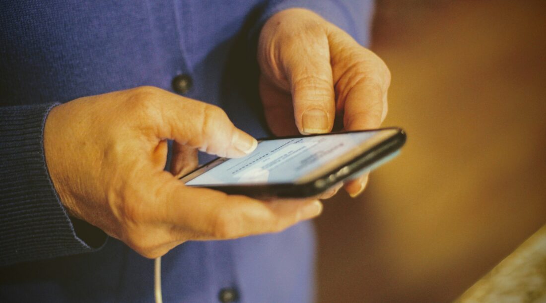 An older person in a blue shirt is holding a smart phone