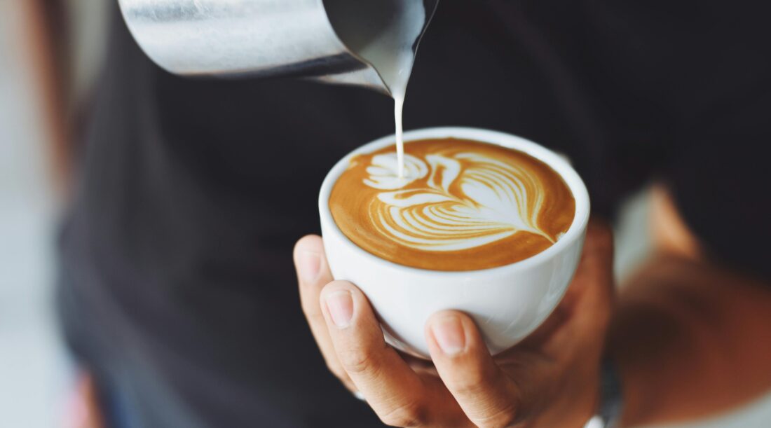 A person pours milk into coffee to create latte art