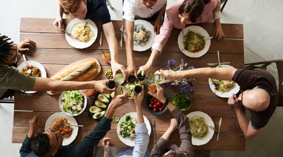 Overhead shot of many people toasting glasses over a dinner table