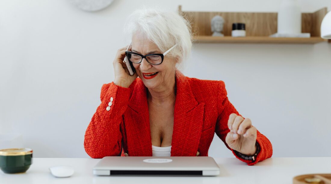 An older woman smiles while holding a phone to her ear