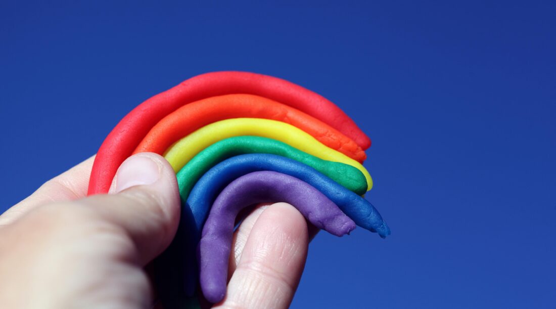 A hand holding a rainbow sculpted out of clay