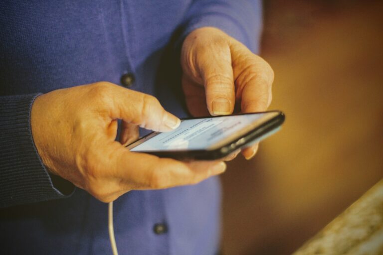 An older person in a blue shirt is holding a smart phone