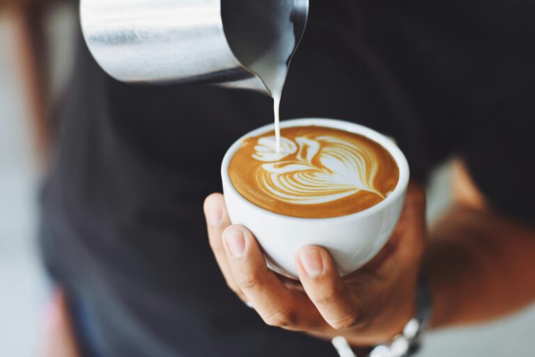 A person pours milk into coffee to create latte art