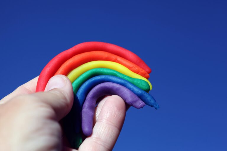 A hand holding a rainbow sculpted out of clay