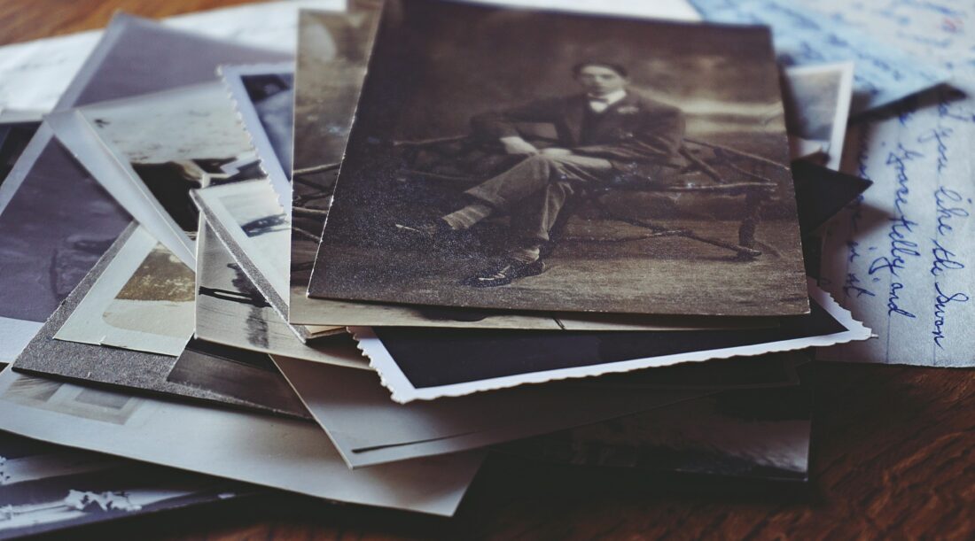 A pile of old letters and photographs, with a black and white photograph of a man in a suit on top