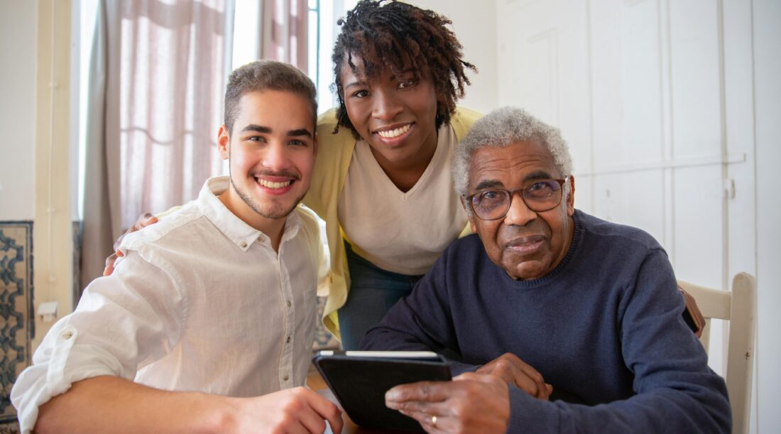 Two young people and an older man holding a tablet sit at a table