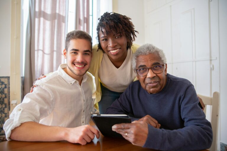 Two young people and an older man holding a tablet sit at a table