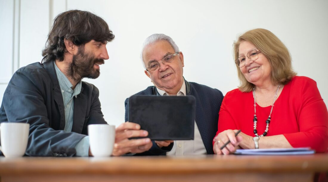 A younger man shows a tablet to an older man and woman