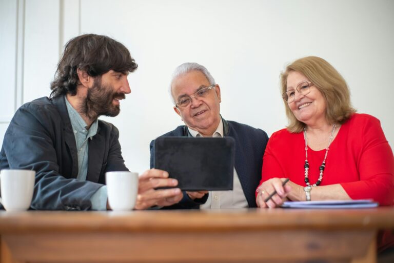 A younger man shows a tablet to an older man and woman